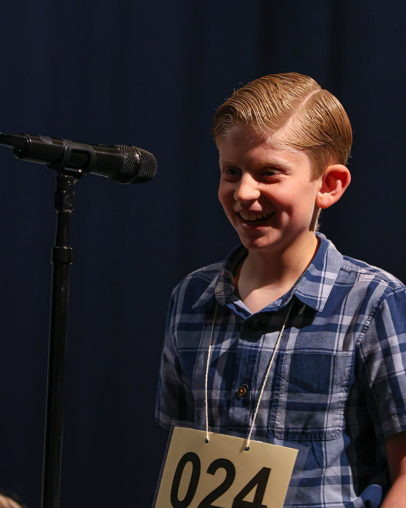 A student standing next to a microphone smiles to the left. 