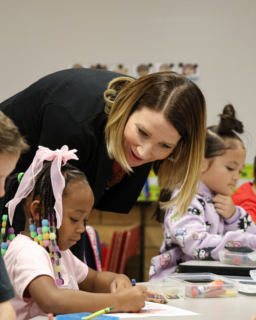 a principal leaning down and talking with a student as they color. 
