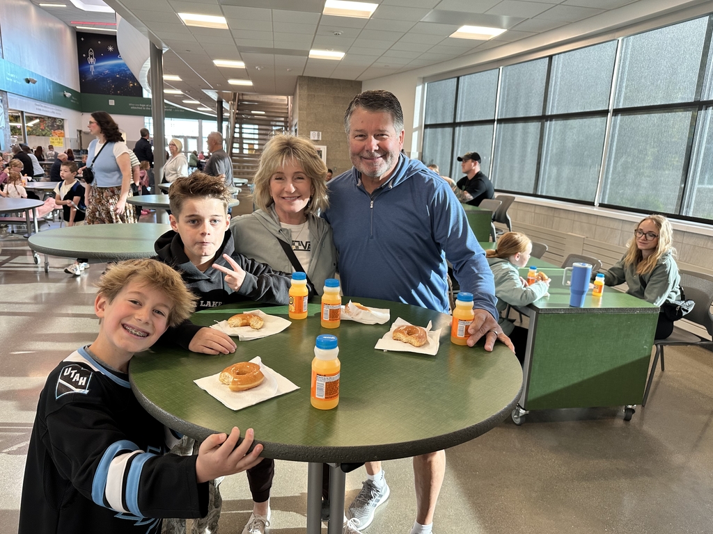 two boys with lady and man standing around a table holding the peace sign smiling with donuts and orange juice