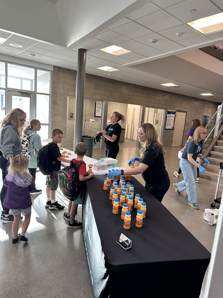 women standing behind black table handing out donuts and orange juice to children and a women