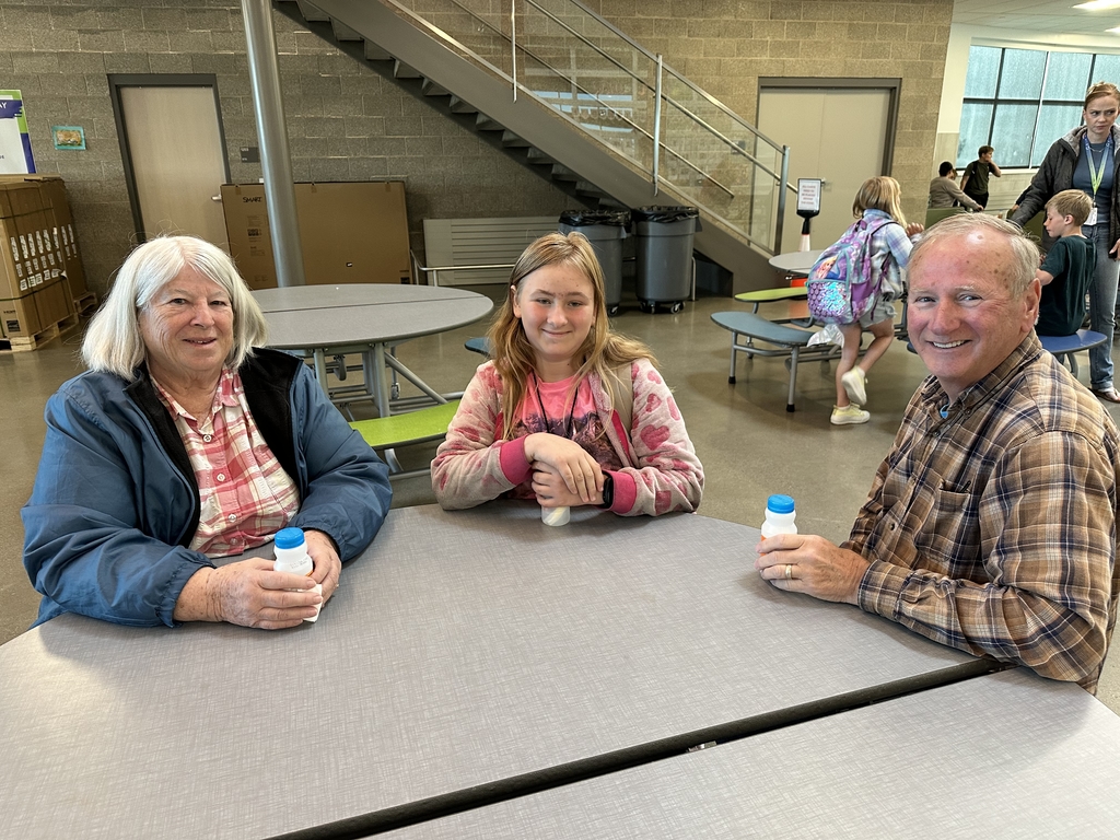 young girl  sitting between a older lady and older gentlemen holding orange juice bottles