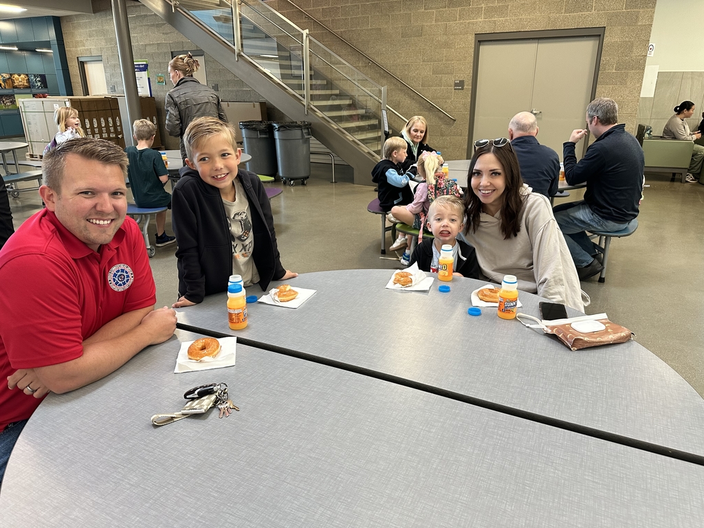 two boys and two adults sitting around a table with donuts and orange juice