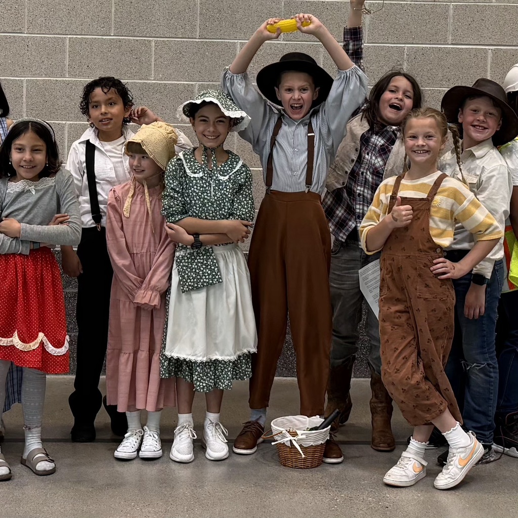 Bountiful Elementary fourth grade students pose together in pioneer-style costumes after their Utah history program. Several students wear bonnets, hats, suspenders, dresses, and vests while smiling and celebrating.