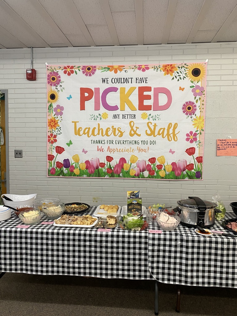 image of a table covered in food and a sign hanging on the wall behind the table. sign says we couldn't have picked any better teachers & staff thanks for everything you do! we appreciate you! sign has flowers on it.