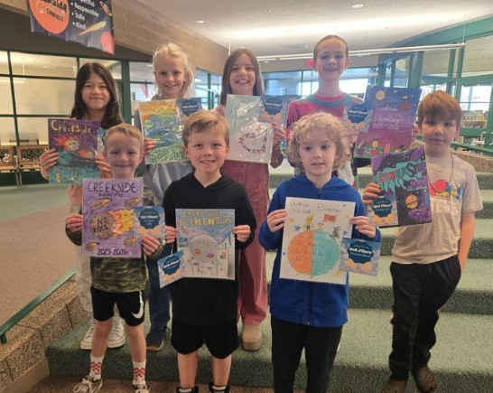 STUDENTS HOLDING YEARBOOK COVER THEY DREW FOR CONTEST