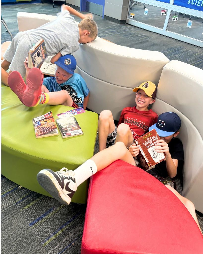 Two students laugh while sitting between separated flexible seating cushions with books in hand during a funny classroom moment.