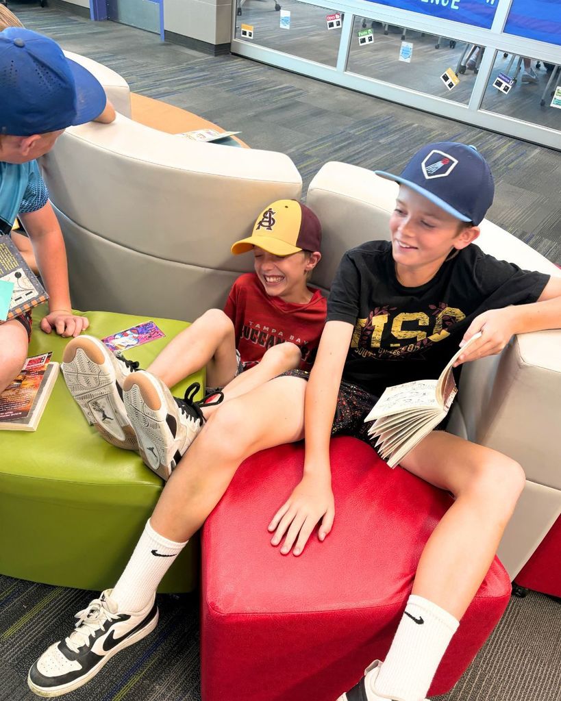 Two students laugh while sitting between separated flexible seating cushions with books in hand during a funny classroom moment.