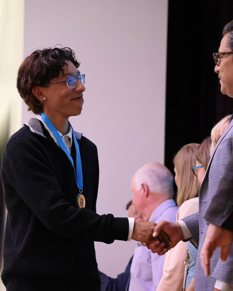 A smiling student shakes the hand of Assistant Superintendent Dr. Fidel Montero.