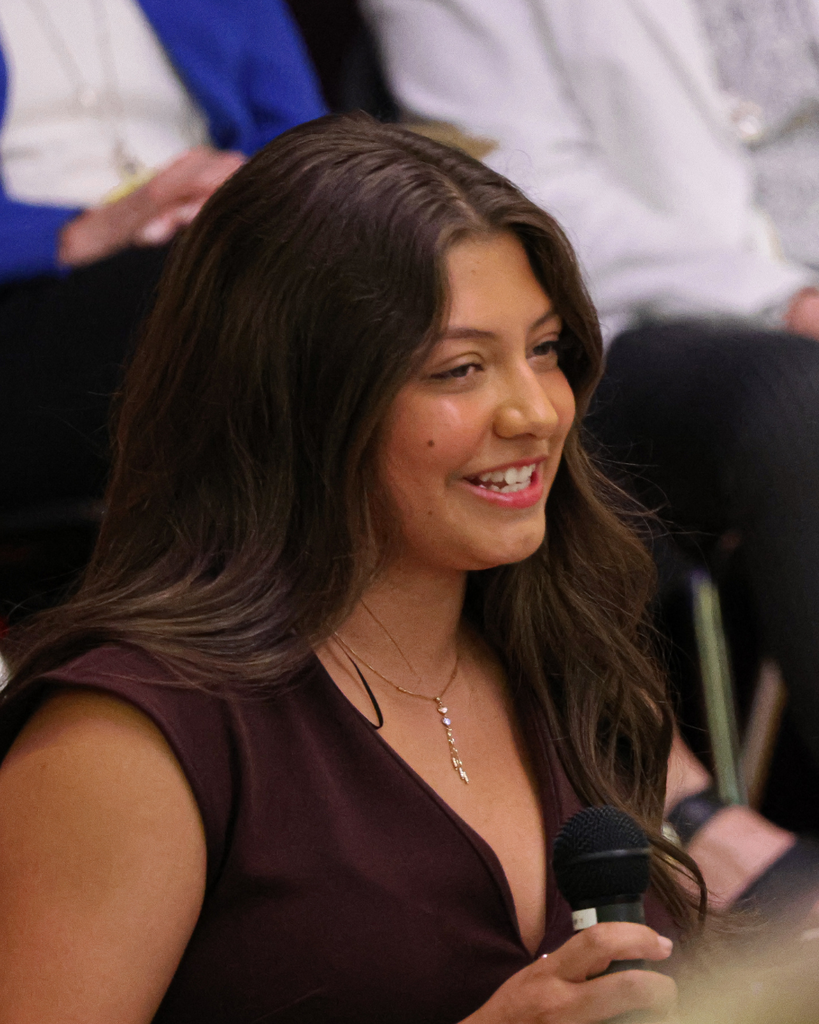 A smiling student looks to the right while holding a microphone.