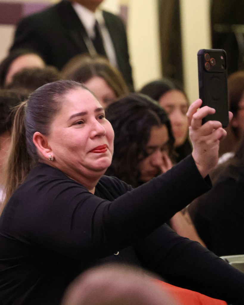 A guardian holds up her phone to record a video. She is visibly moved. 