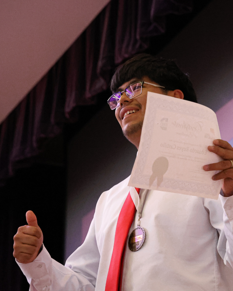 A student holding a certificate smiles and gives a thumbs up. 