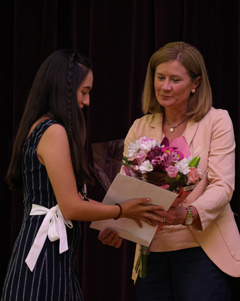 An adult hands a student a bouquet of flowers.
