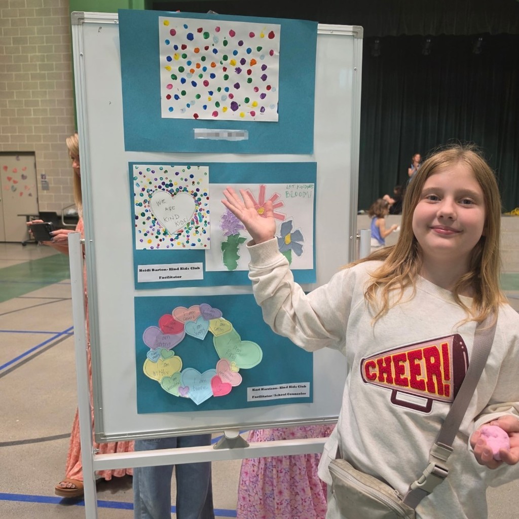 Bountiful Elementary student stands beside colorful kindness artwork created for the final Kind Kids Club art exhibit.