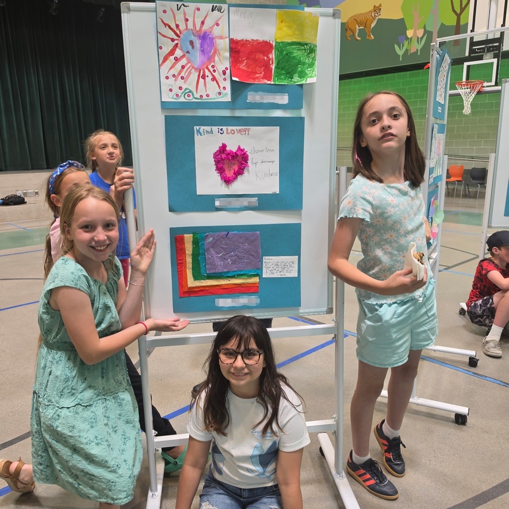 Bountiful Elementary students pose with kindness-themed artwork during the final Kind Kids Club art exhibit for families.