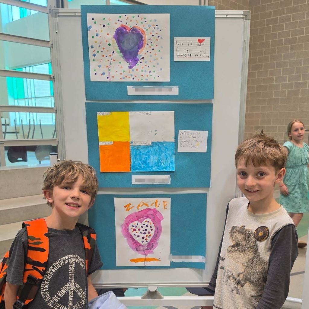 Bountiful Elementary students stand beside colorful kindness artwork created for the final Kind Kids Club art exhibit.