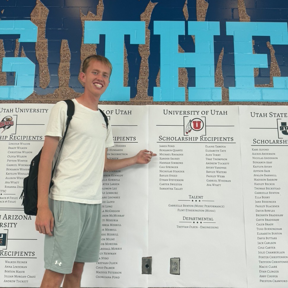 A male student points out their name on the scholarship wall
