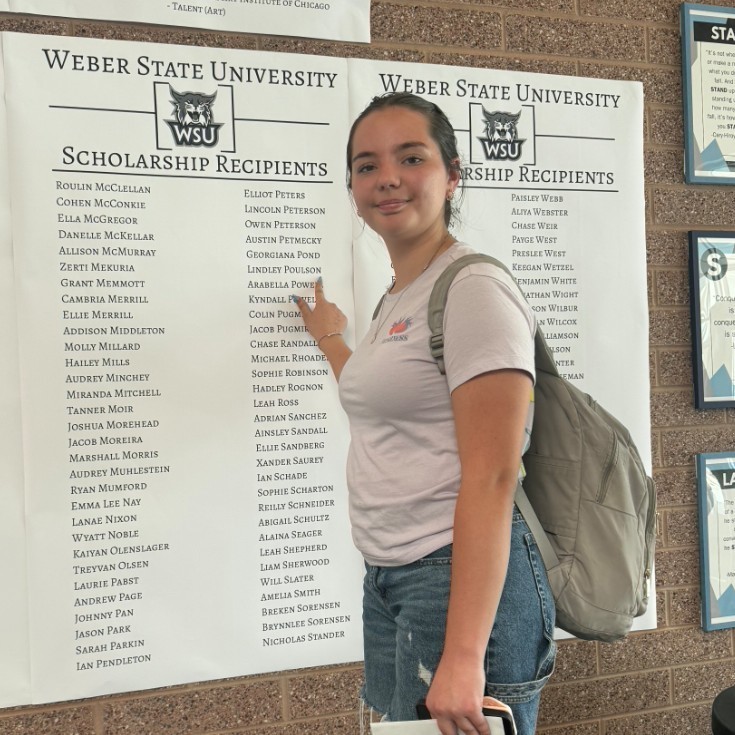 A female points to her name in the scholarship wall