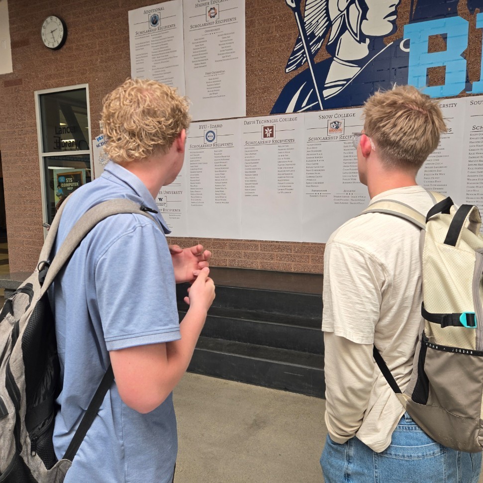 Two male students looking at all of the scholarships on the wall