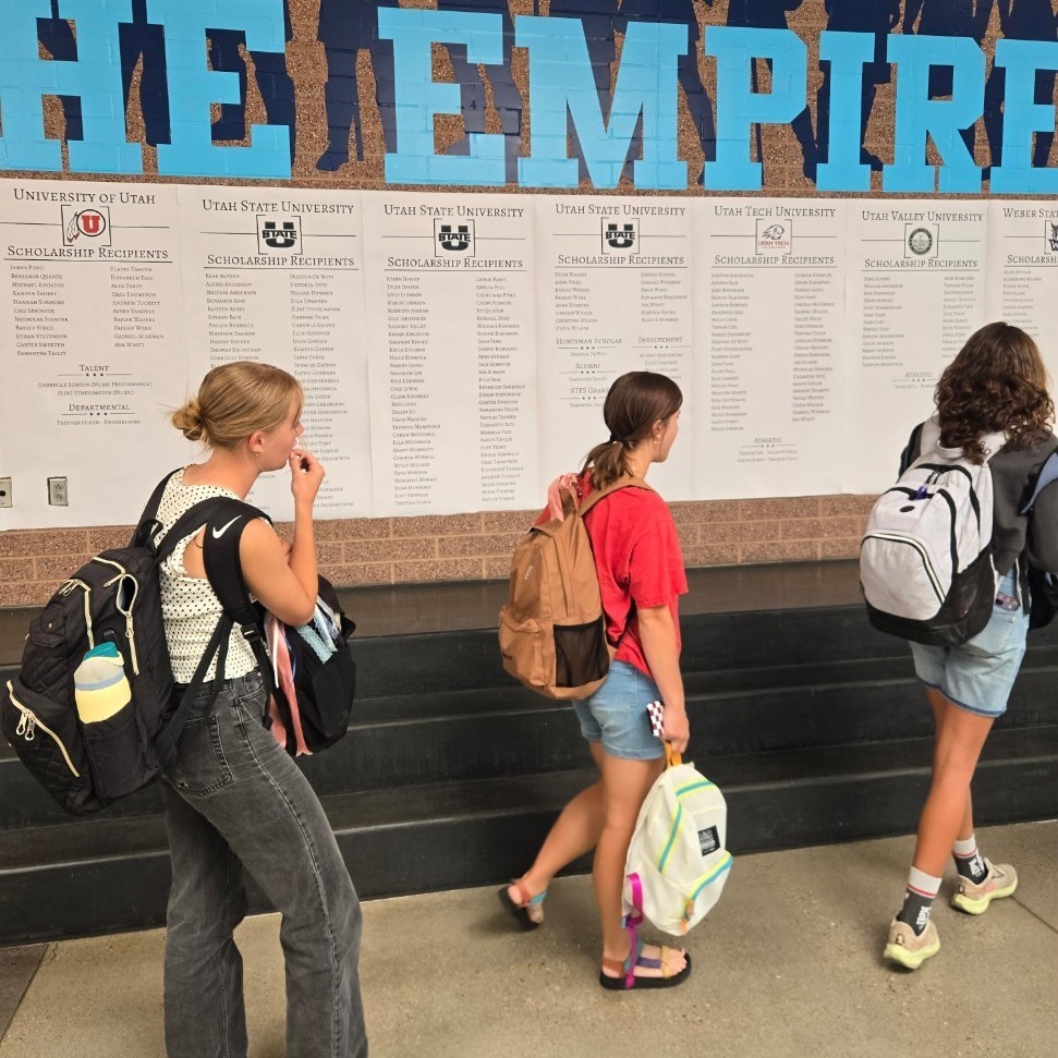 Three female students looking for names on the scholarship wall