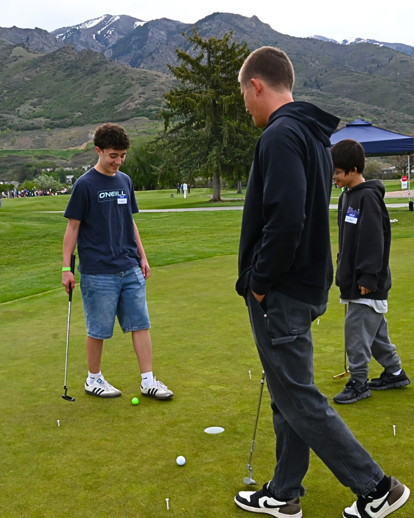 Three students smile as they look at their golf balls on the course. 