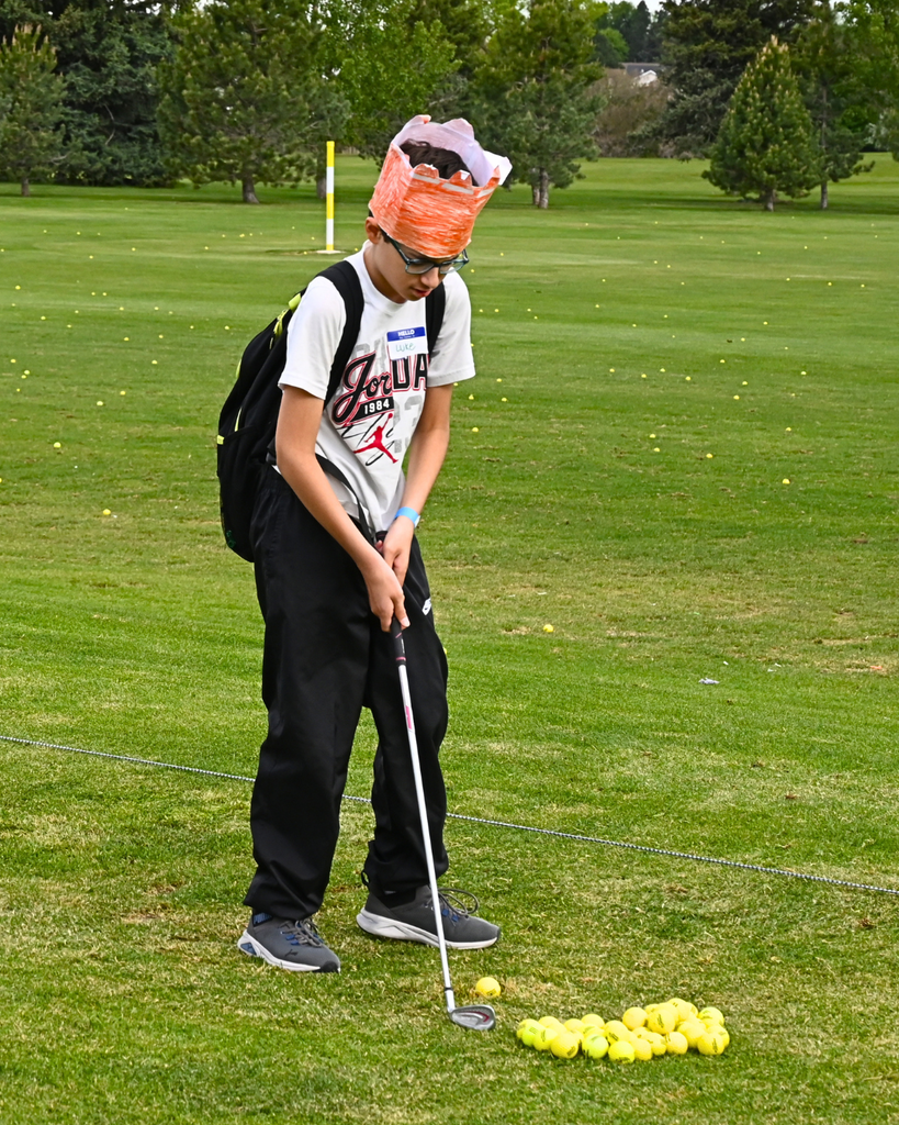 A student wearing an orange colored paper crown gets ready to putt. 