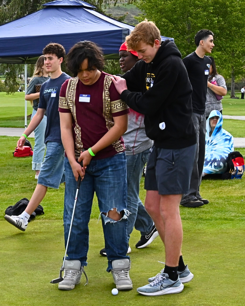 A student helps another student hit their golf ball.