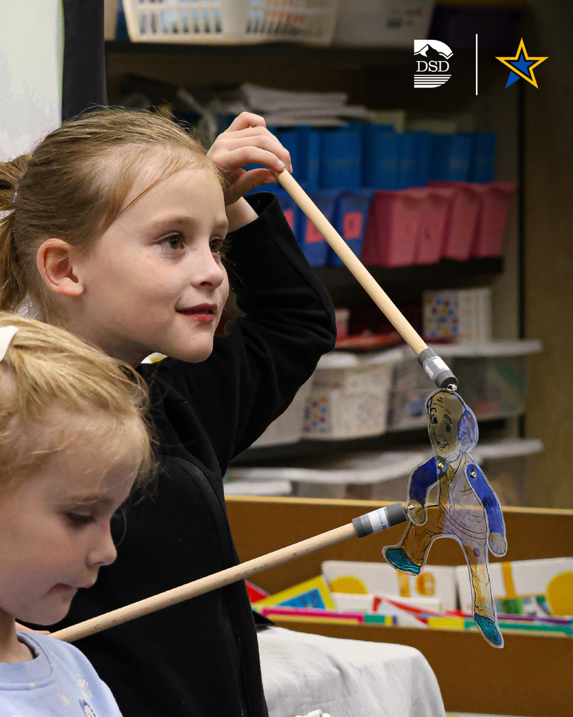 A student holding up a shadow puppet with sticks.