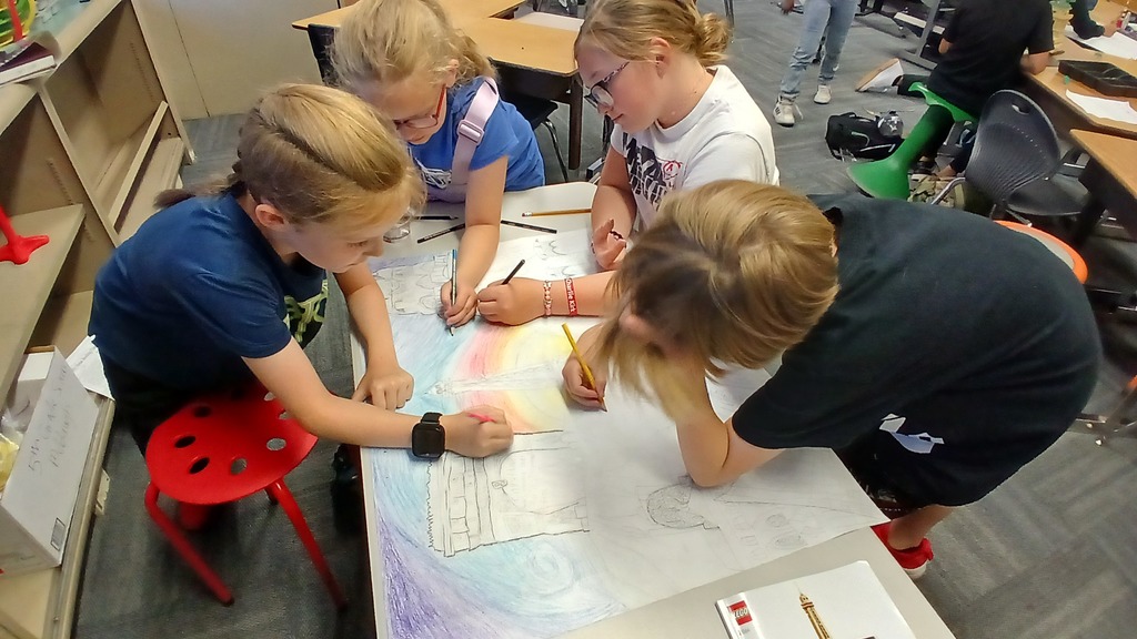 Four young students leaning over a large table, collaborating on a colorful hand-drawn poster that includes a drawing of a tower.