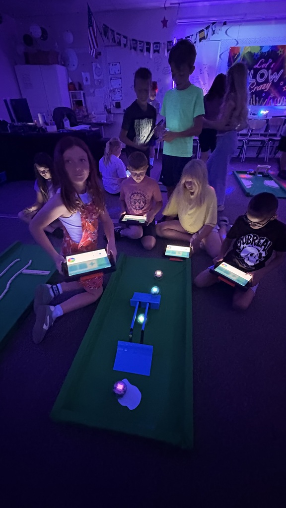 four students using ipads sitting around a golf course simulator