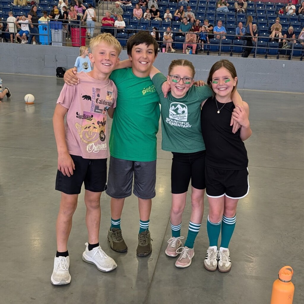 Four Bountiful Elementary students pose together at the district Decathlon event inside a large indoor athletic facility.