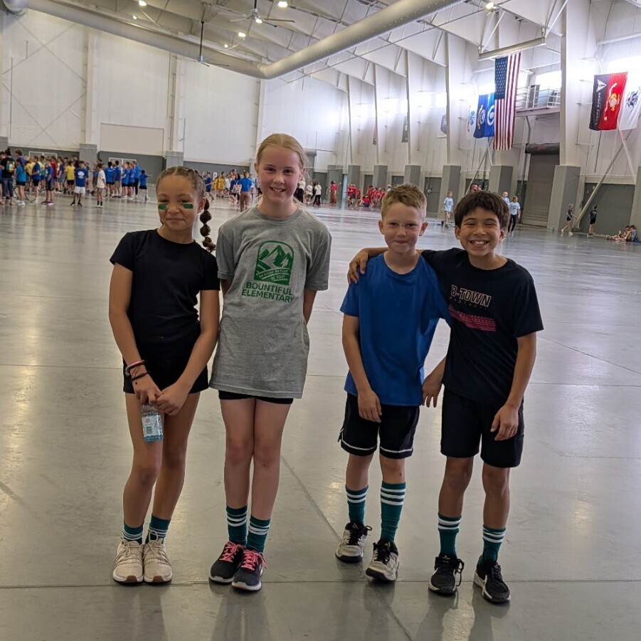 Four Bountiful Elementary students pose together at the district Decathlon event inside a large indoor athletic facility.
