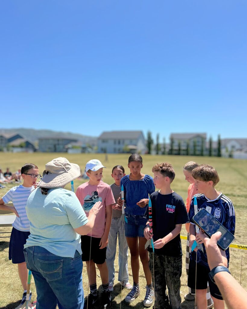 Students gather in a grassy field holding rockets while listening to launch instructions before sending their rockets into the air during the 6th grade STEM activity.