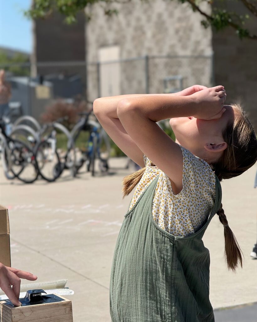preparing for a rocket launch during the 6th grade STEM activity. The launch area and bike racks are visible in the background on a sunny day.
