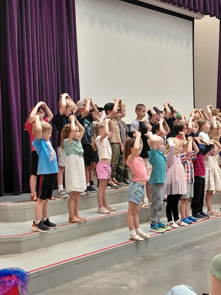 Kindergarten performing their end of year program on the stage in front of parents. 