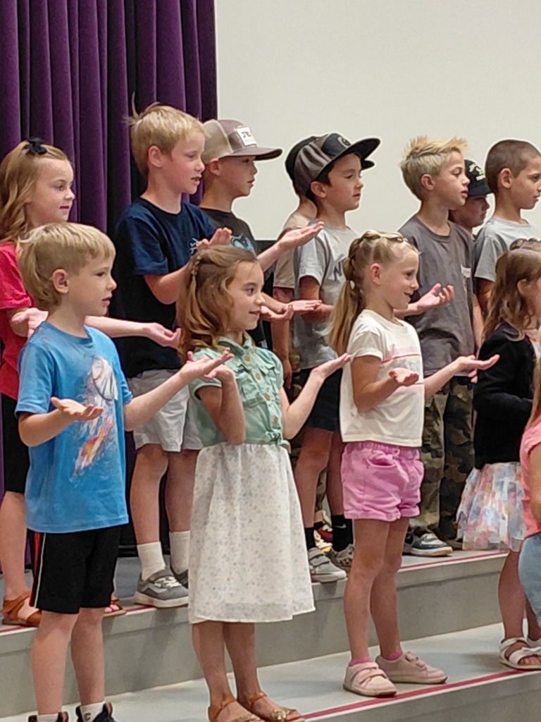 Kindergarten performing their end of year program on the stage in front of parents. 