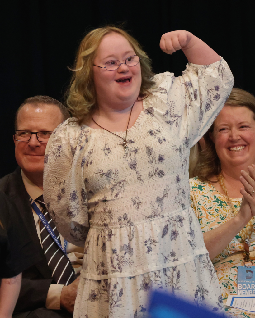 A Vista Education Campus graduate smiles while lifting up her hand.