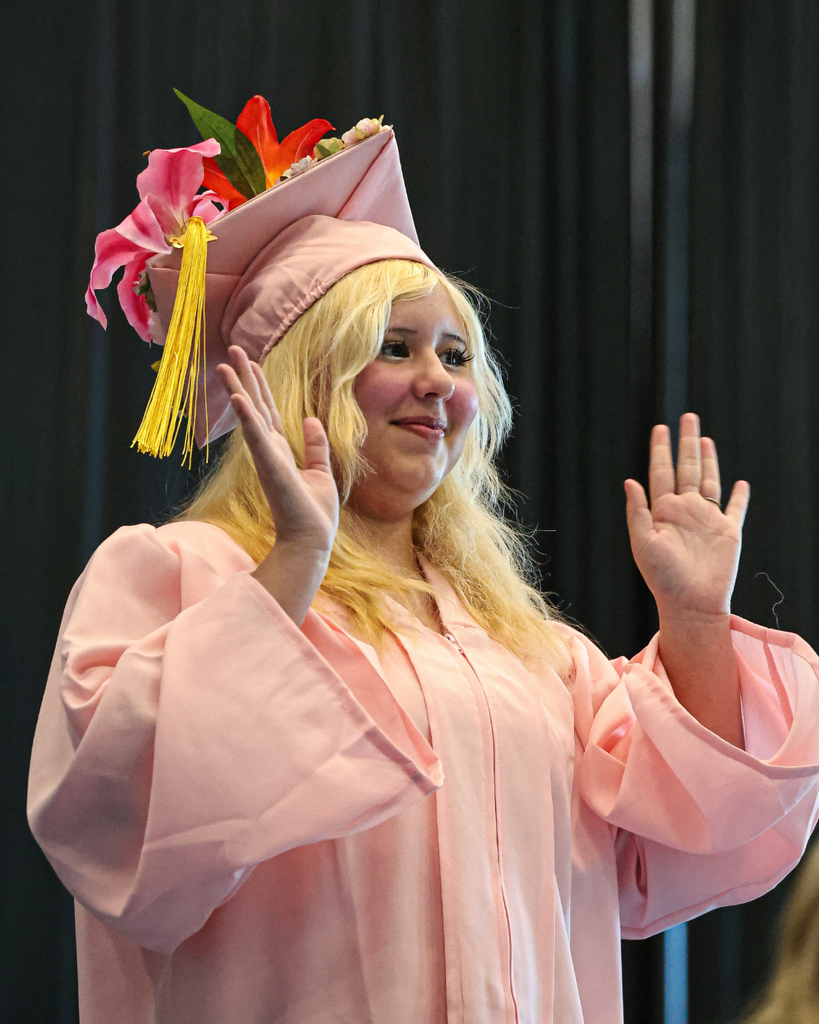 Davis Adult Education graduate in a pink cap and gown waves to the audience.