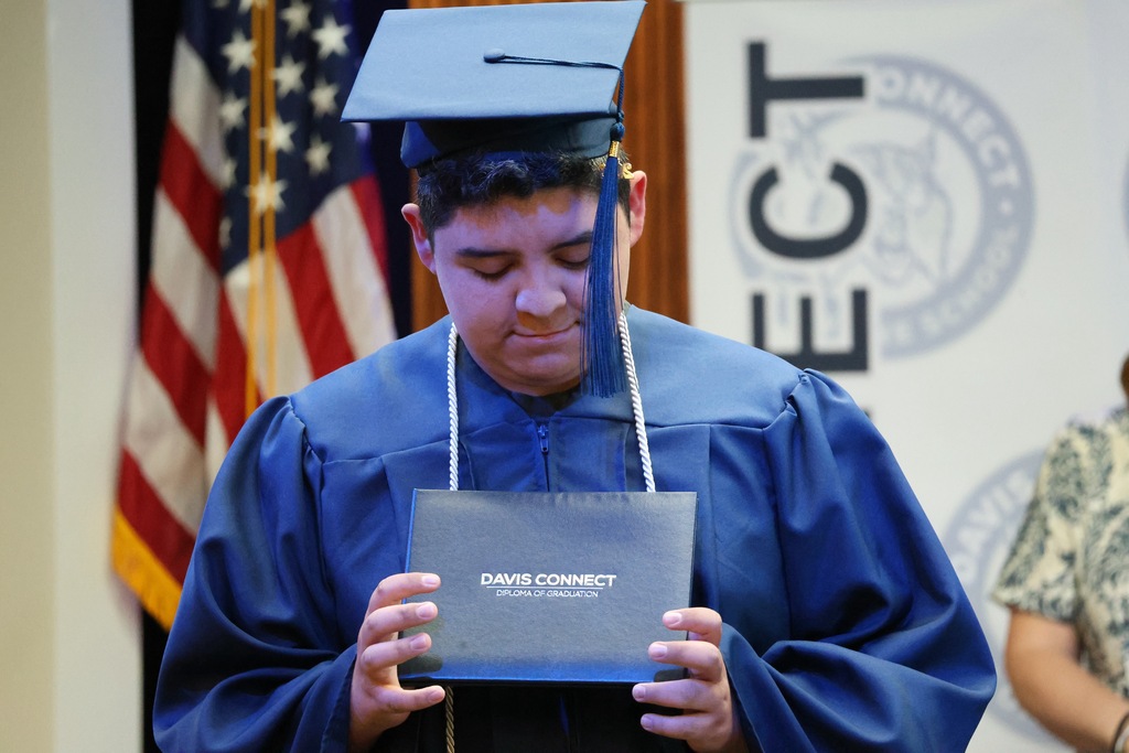 A Davis Connect graduate looking down at their diploma cover. 