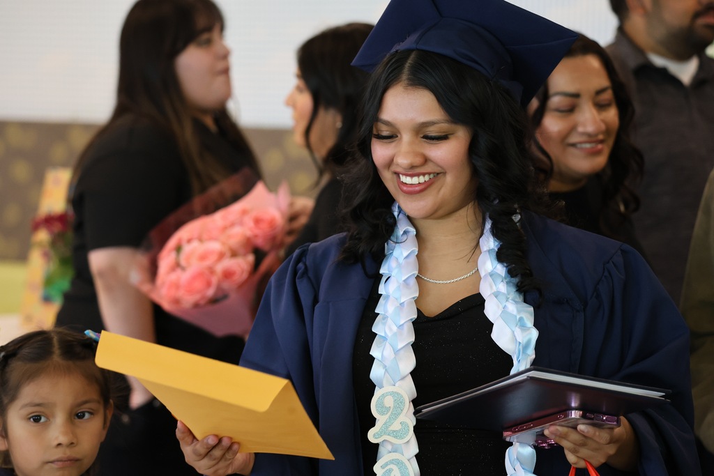 A Davis Connect graduate smiling while looking at their diploma cover. 