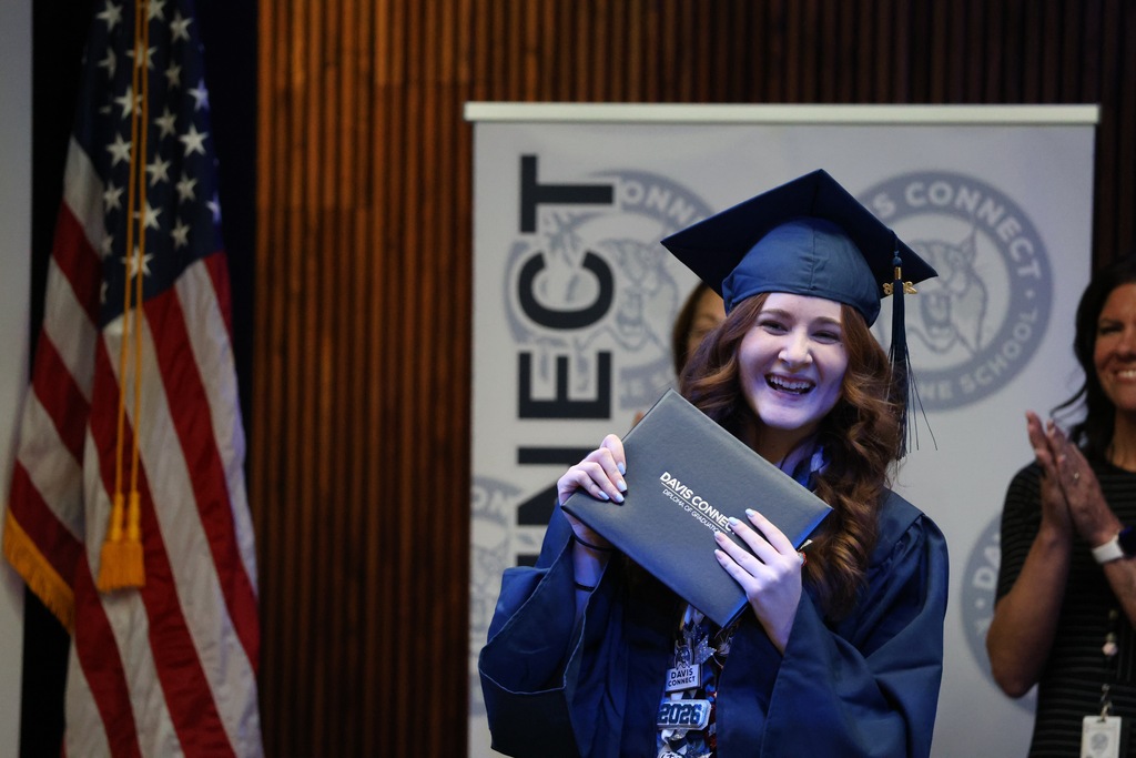 A Davis Connect graduate smiling while holding their diploma cover. 