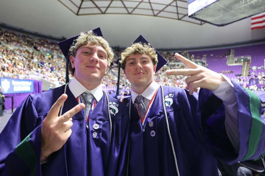 A Syracuse High graduates smile at the camera and give peace signs.