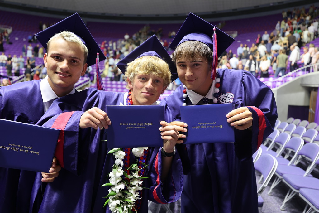 Woods Cross graduates smile at the camera while showing their diploma covers.