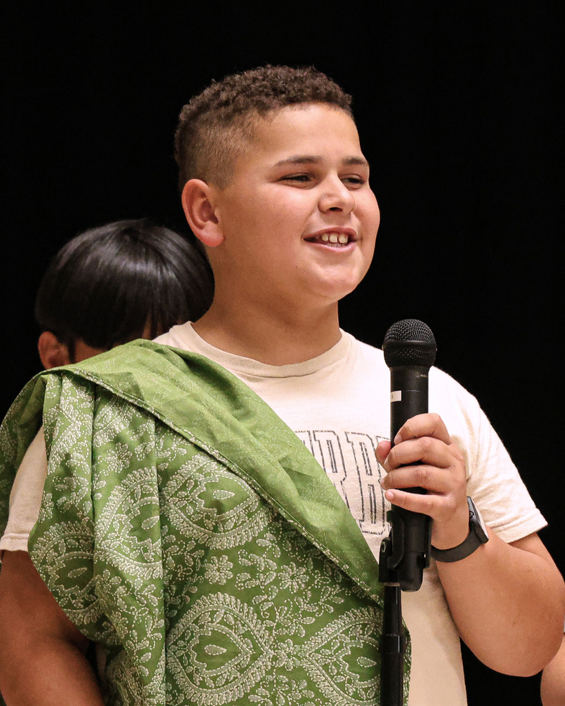 A Foxboro student wearing a green robe speaks into the microphone.