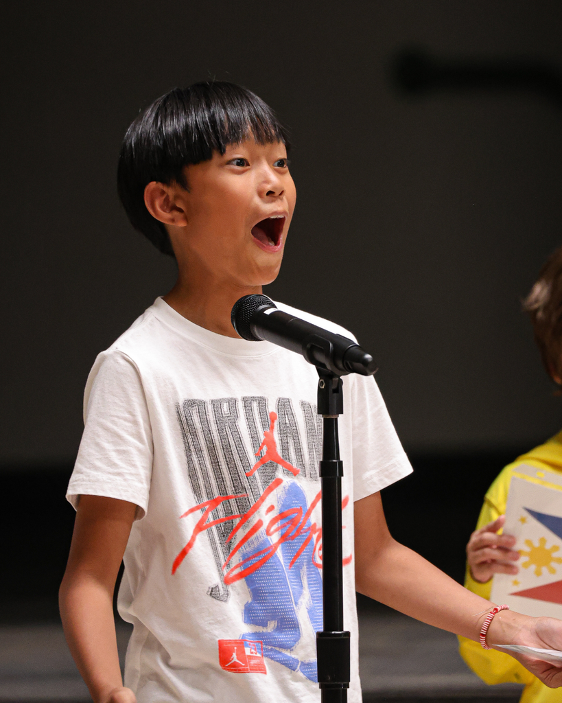 A student standing in front of a microphone looks surprised.