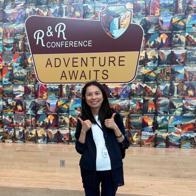 teacher posing in front of a mural that says R & R Conference