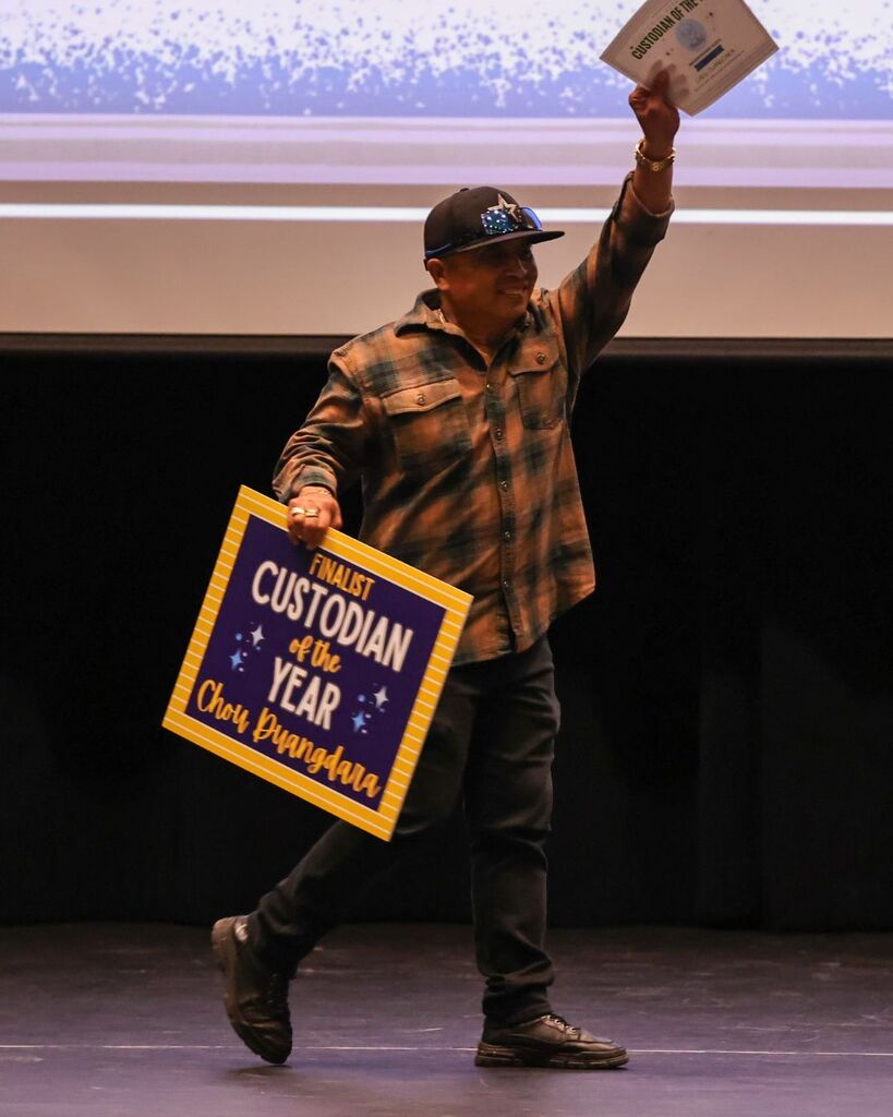 A custodian smiles while holding up a sign that reads: "Finalist Custodian of the Year Chou Duangdara."