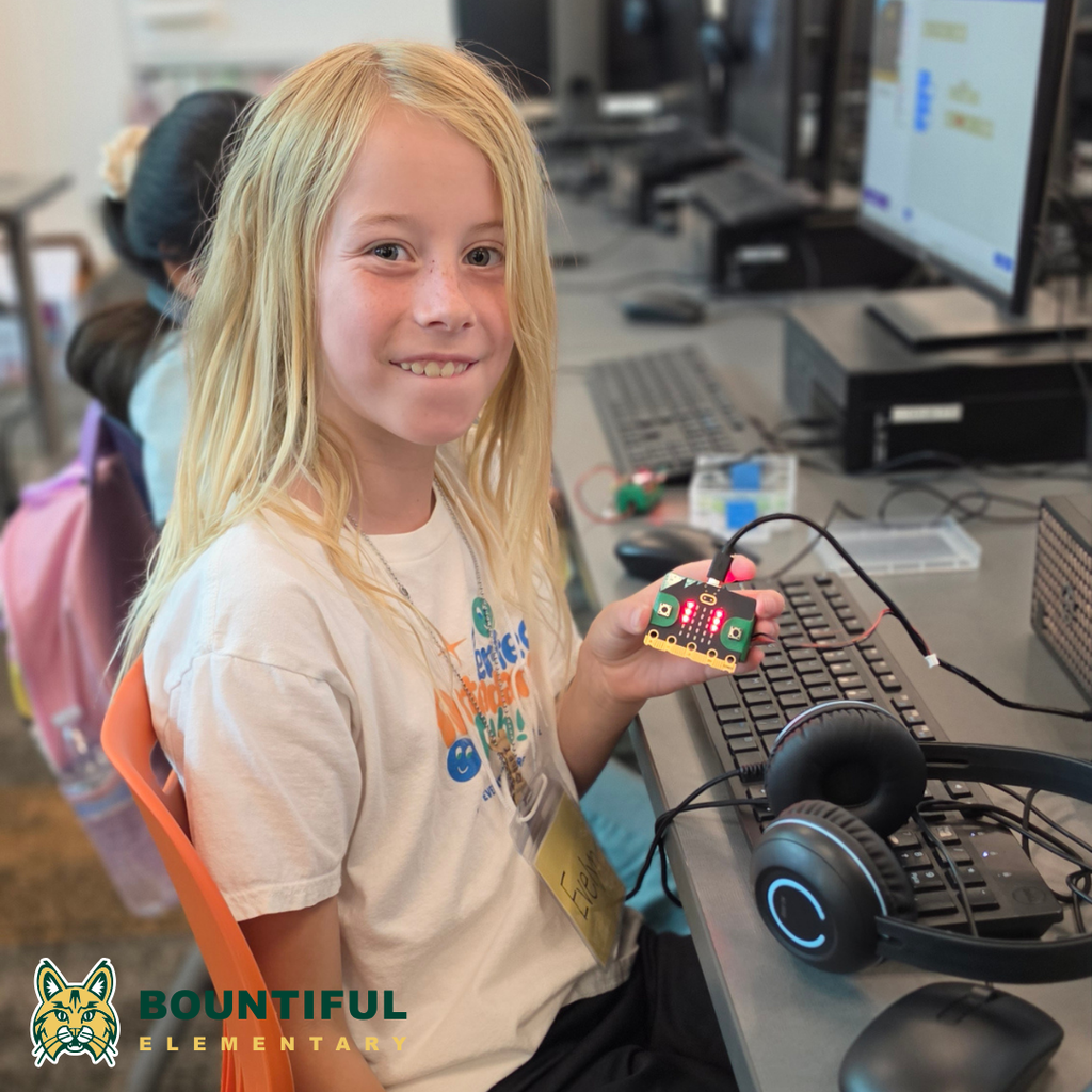 Bountiful elementary student smiling while holding a lit micro:bit connected to a computer during summer school.