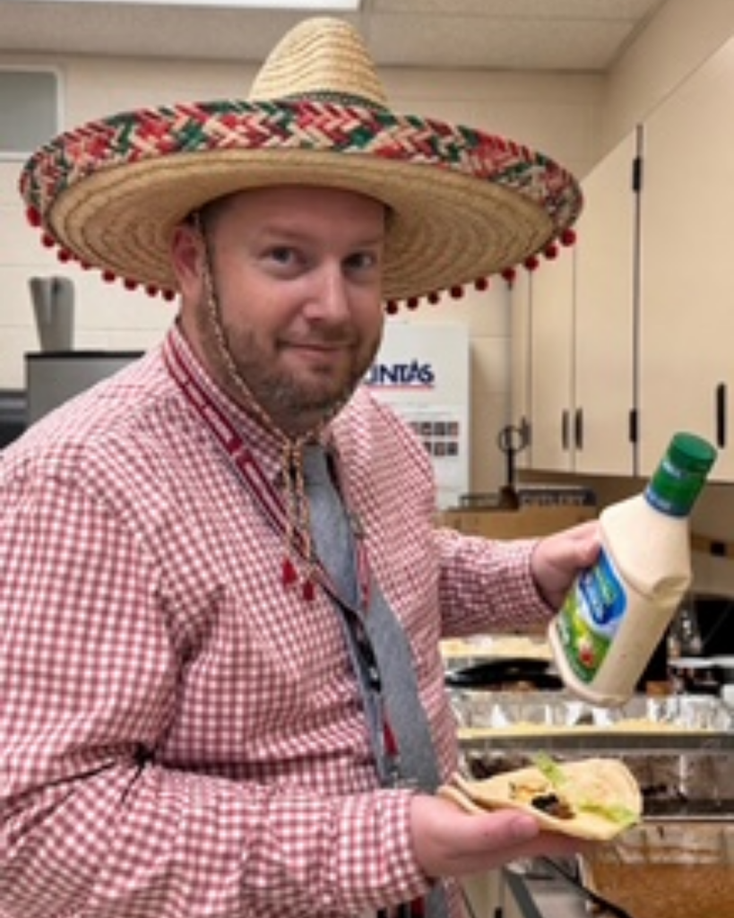 A man in a sombrero holding a taco and ranch.
