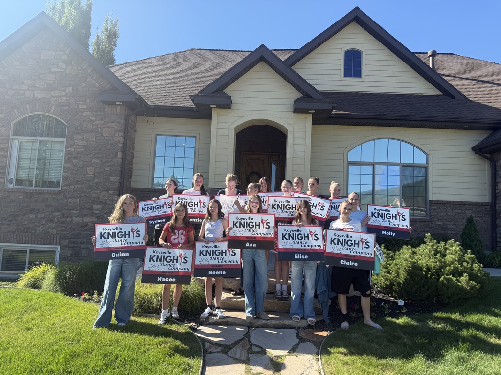 image of girls holding kaysville knight'syard signs. standing in front of a house.