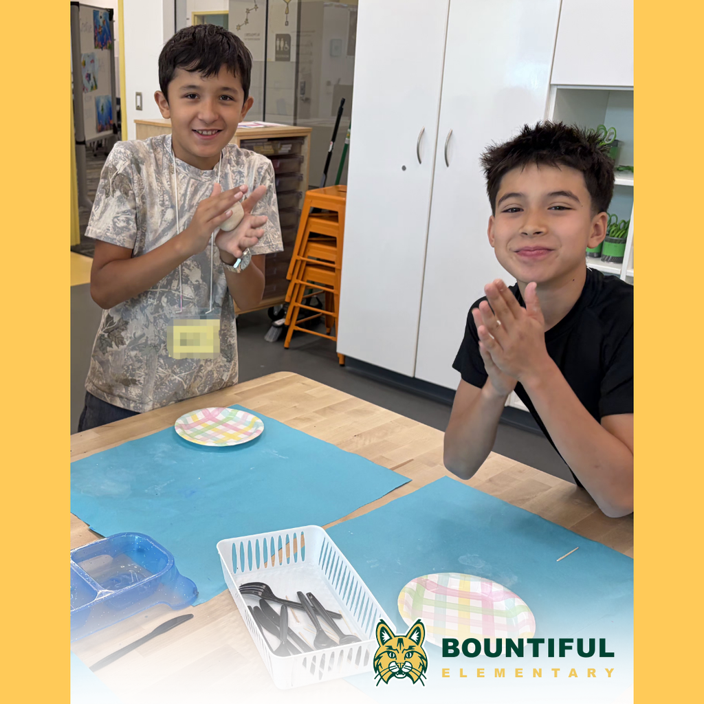 Two Bountiful elementary student smile while shaping air-dry clay at a classroom table.